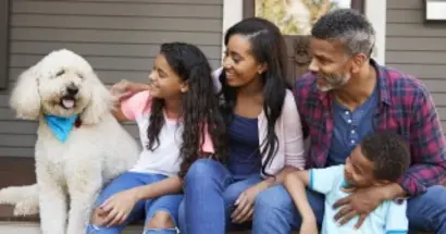 A Black family of 3 sitting on the porch of their home with their fluffy white dog.