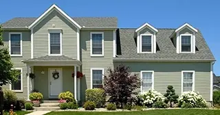 A two story home with light gray siding and white trim, framed by trees and landscaping. 