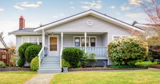 A single-family one-story home with gray siding, white trim, a porch, landscaping and lawn.