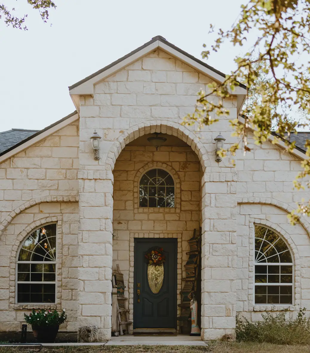 Entrada alta a una gran casa de piedra con exterior beige y decoraciones de porche estilo suroeste.