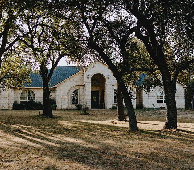 A large home featuring a tall entryway with beige stone exterior walls set in a property full of mature trees.