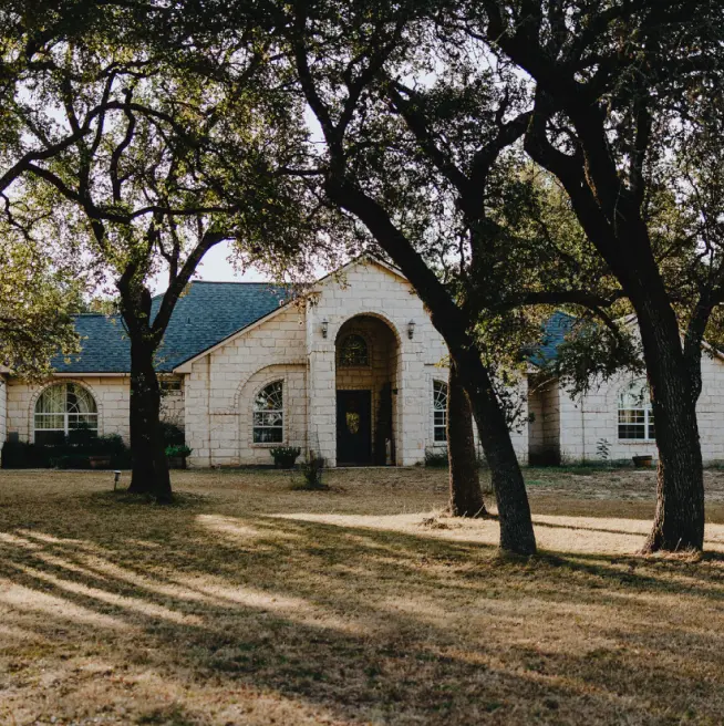 A large home featuring a tall entryway with beige stone exterior walls set in a property full of mature trees.