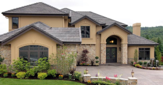 A large home featuring a tall entranceway, with beige stone exterior walls, tan siding, and multiple dark brown gabled roofs.