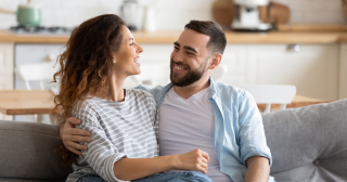 A couple in their mid-30s enjoy a laugh together on their couch.