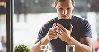 A young adult man in a gray t-shirt reads about refinancing on his phone. 