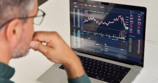 A middle-aged white man with glasses and salt-and-pepper hair contemplates a laptop screen with a picture of a graph.