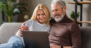 A middle-aged white couple cuddle together on a couch while looking at a laptop.