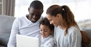 Mixed race family sitting on a couch and looking at a laptop.