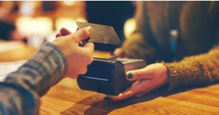 A woman's hand presents a credit card to pay for a transaction.