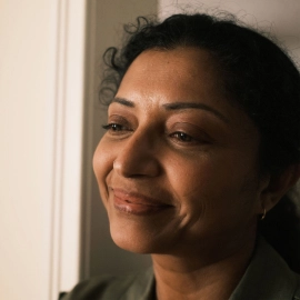 A hispanic woman looks into the distance while smiling.