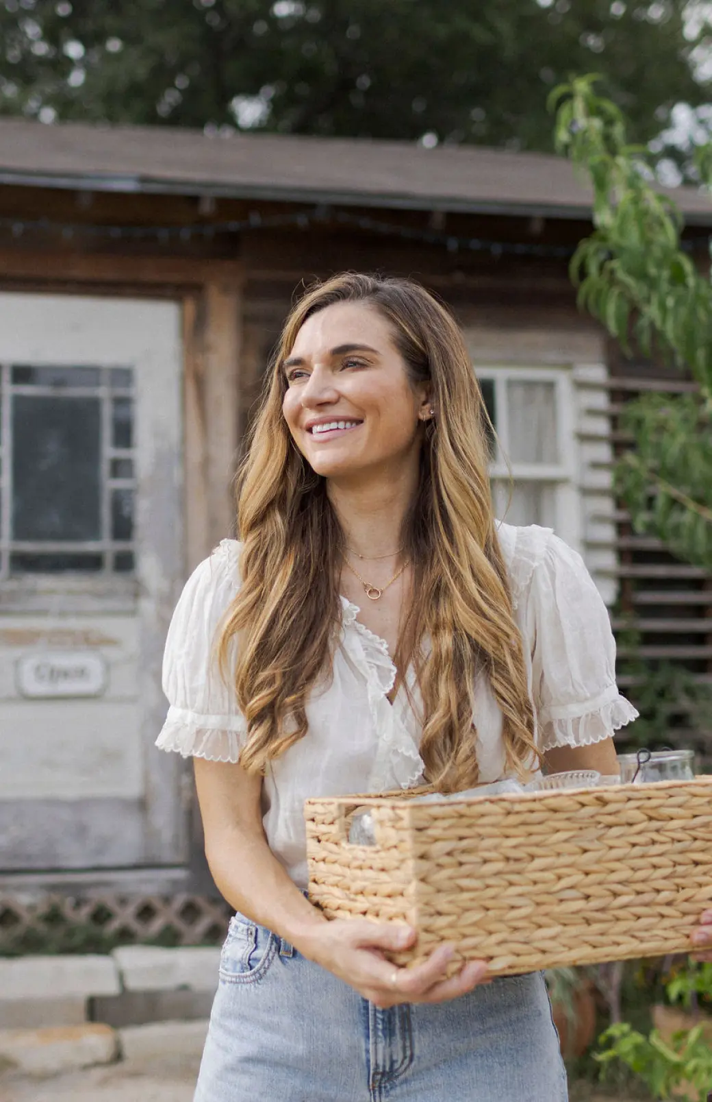 A white woman stands in front of her small business, holding a basket of handmade goods.