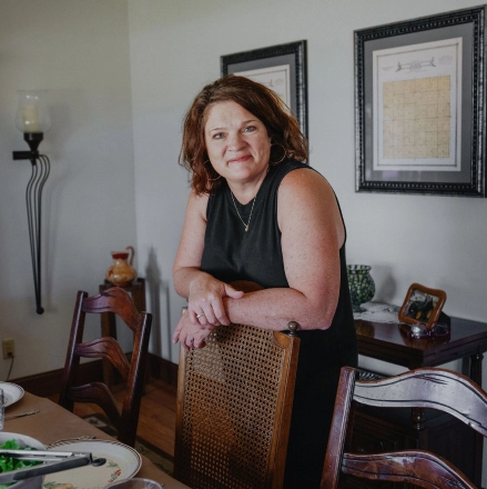 A white woman leaning over a dining room table set with food for a family meal.