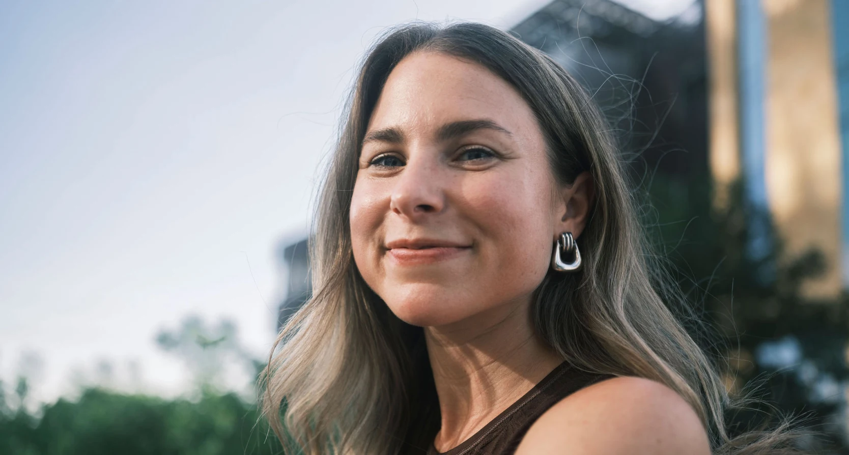 A white woman in her 40s with long brown hair smiles at the camera.