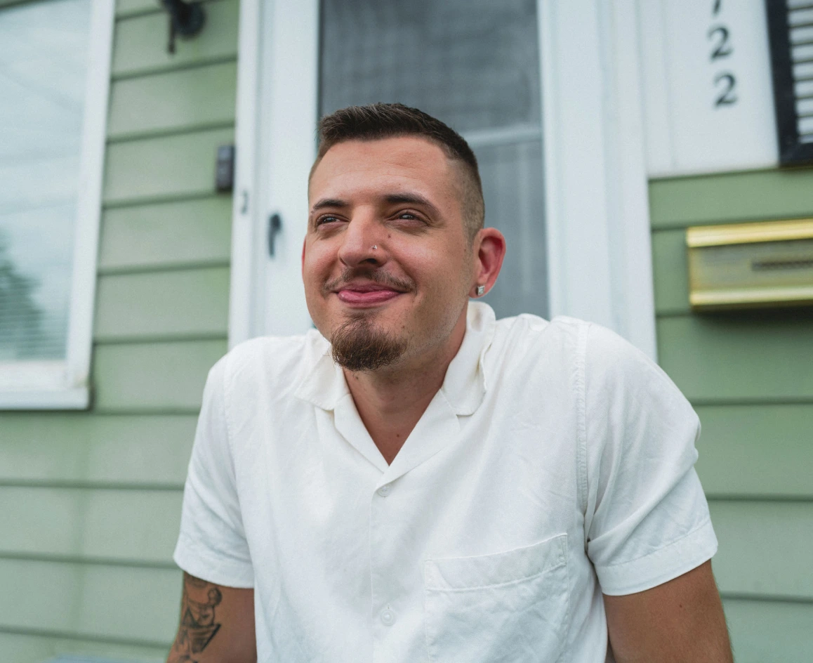 Rocket Mortgage has a wide variety of options to help home buyers like this man in his 30s wearing a white polo shirt and sitting on the front porch of a home with light green siding.