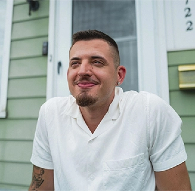 Rocket Mortgage has a wide variety of options to help home buyers like this man in his 30s with a goatee, wearing a white polo shirt and sitting on the front porch of a home with light green siding.