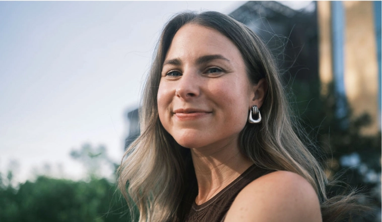 A white woman in her 40s with long brown hair smiles at the camera.