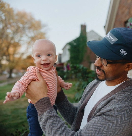 Un padre sostiene a su bebé sonriente frente a su casa.