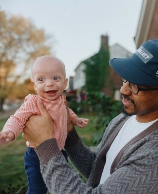 Un padre sostiene a su bebé sonriente frente a su casa.