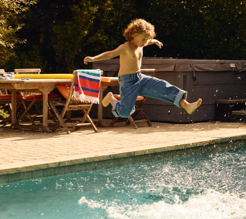 Un niño pequeño salta a una piscina del patio trasero.