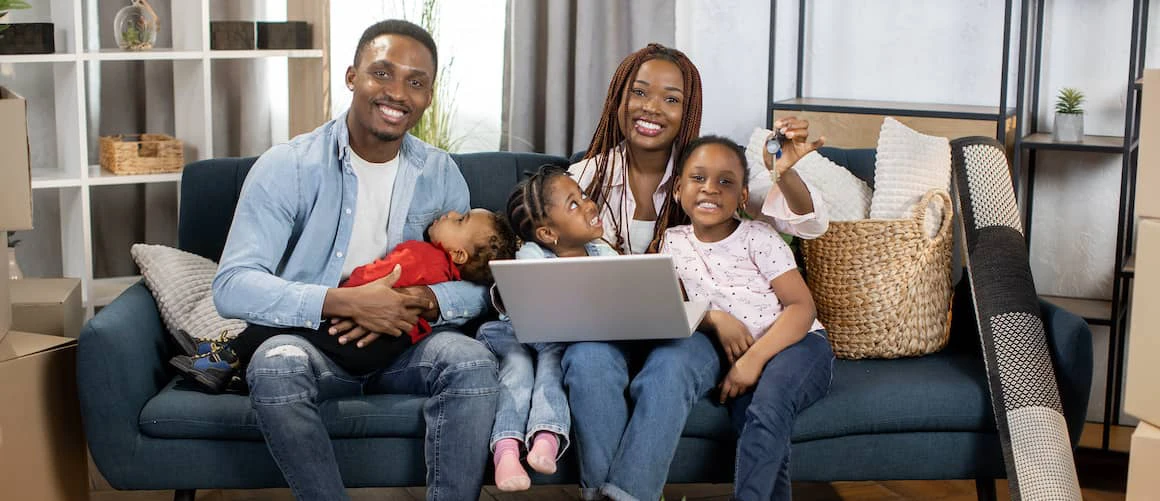 A Black mother and father with their three kids sit on a couch while the mom holds up a set of house keys.