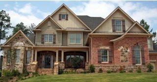 A large stately home with a brick and mixed stone exterior, tan siding and brown shutters.