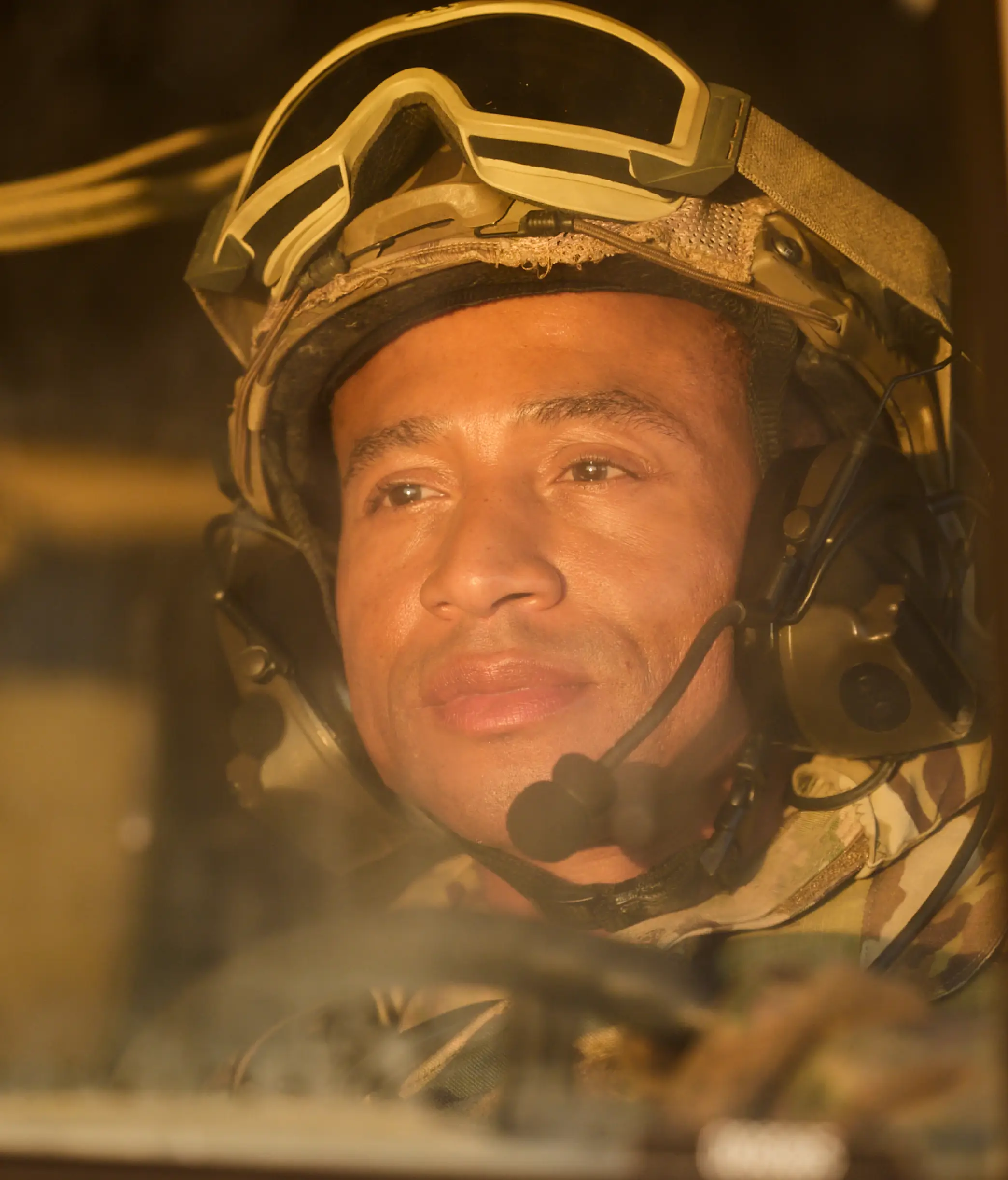 A Black solider in military gear and a headset holds the steering wheel of a vehicle.