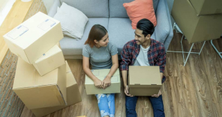 Asian couple looking at each other while sitting on the floor surrounded by moving boxes.