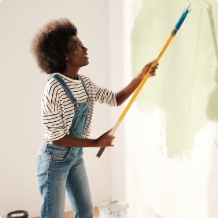 A young black woman in denim overalls painting a wall refinanced with Rocket Mortgage so she could fund home renovations.