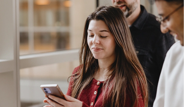 A woman walking with a group of people looks down at her phone.