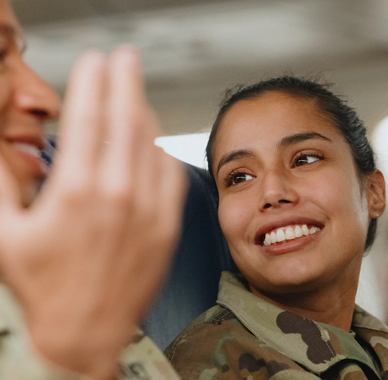 A smiling female service member in uniform chats with another service member during travel.