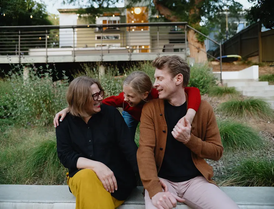 Three adults sitting together outdoors and laughing.