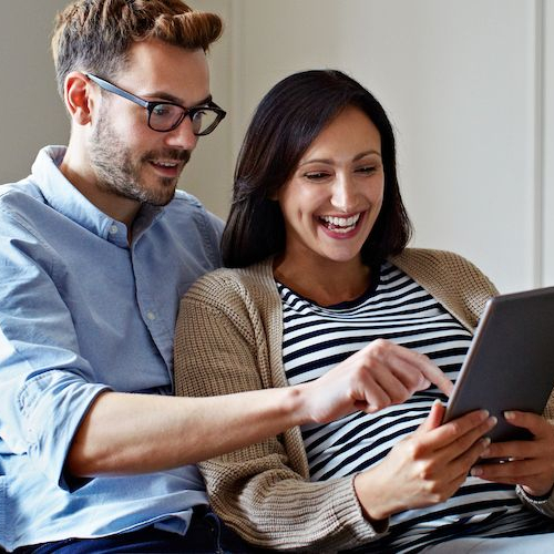 Couple sitting on a couch, having a conversation or relaxing together while looking at something on the tablet.