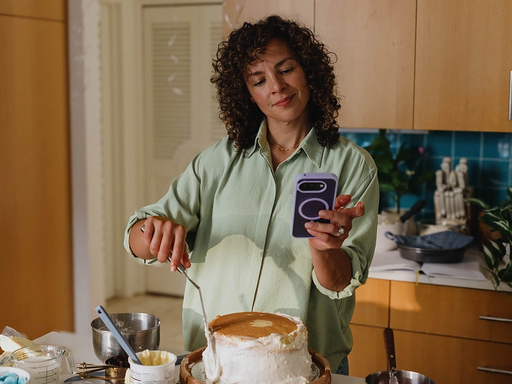 Woman checks her phone while frosting a cake in a her kitchen.
