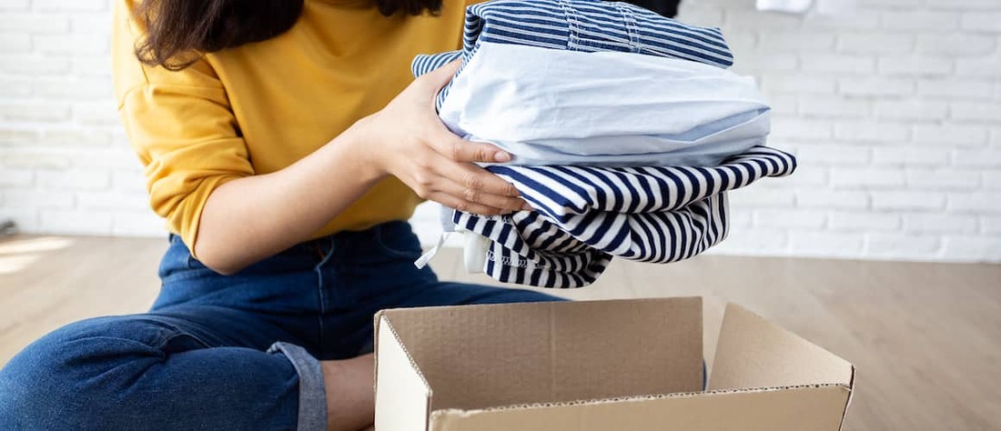 Woman putting folded clothes into a box to donate.