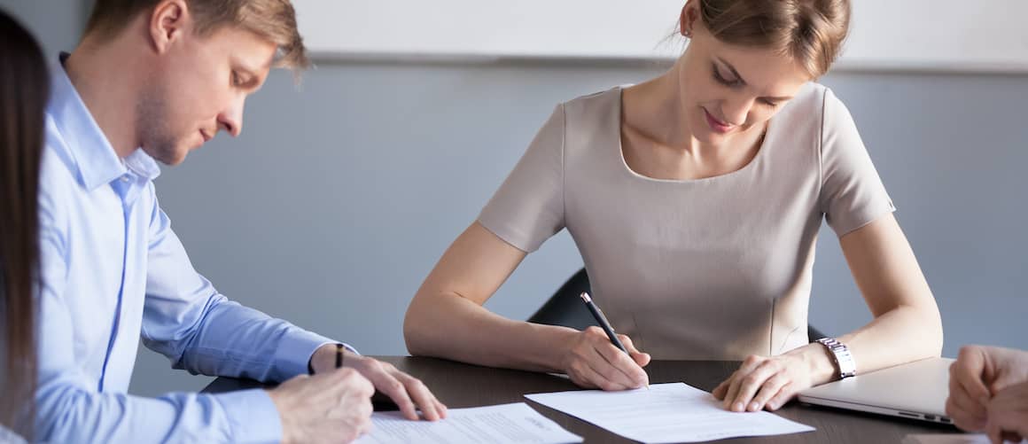 A male and a female business partners signing contracts, suggesting a business or professional agreement.