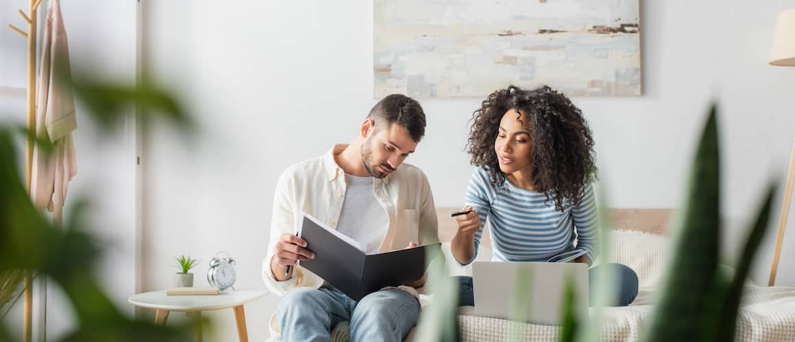 Young couple sitting on the couch together while looking through a folder of files.