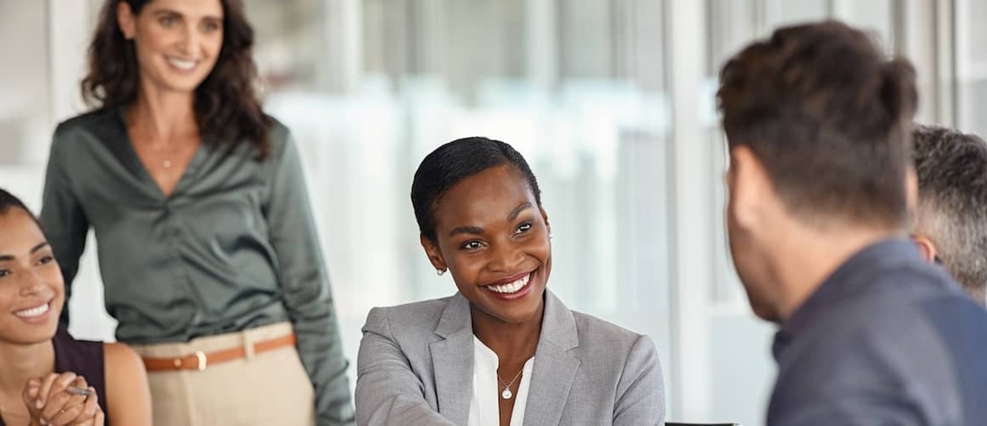 Business woman shaking hands with partner while other female business associates smile   in background.