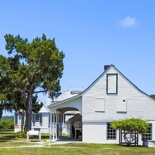 A white house with a spacious lawn and trees surrounding it.