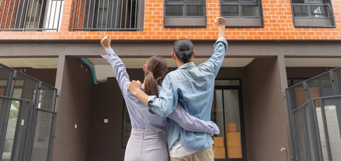 Couple celebrating with arms up outside home.