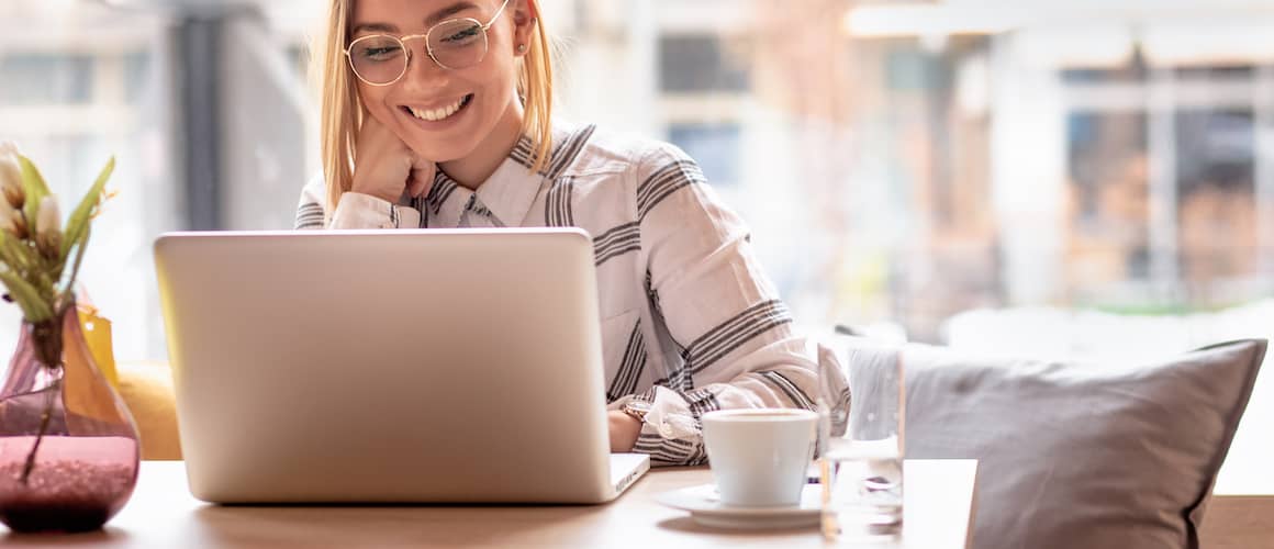 Image of woman at coffee shop, smiling down at computer.