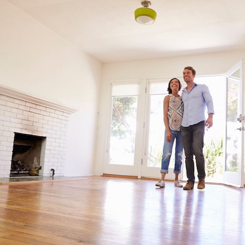 Couple smiling in empty open living room with fireplace.