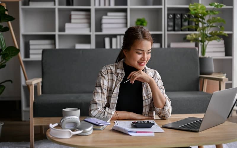 Woman sitting at coffee table with calculator and laptop.