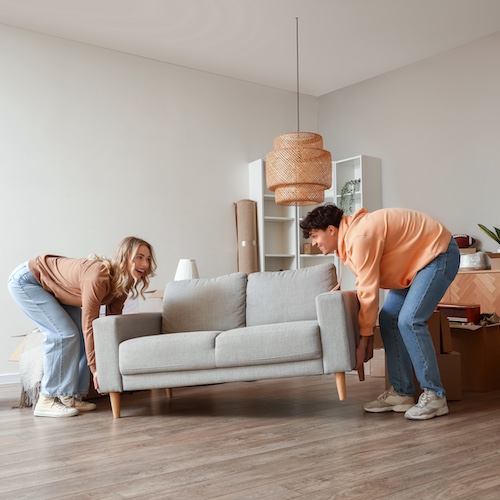 Couple moving grey couch in nearly empty apartment.