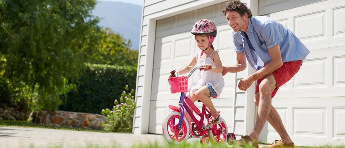 Father teaching daughter to ride bicycle in driveway of home.