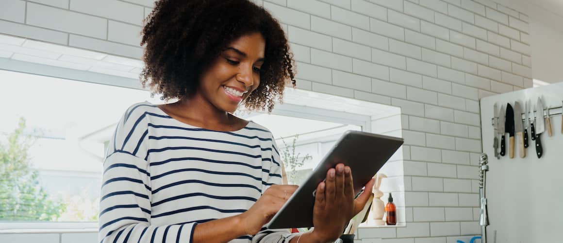 Woman smiles while looking at tablet in her kitchen.