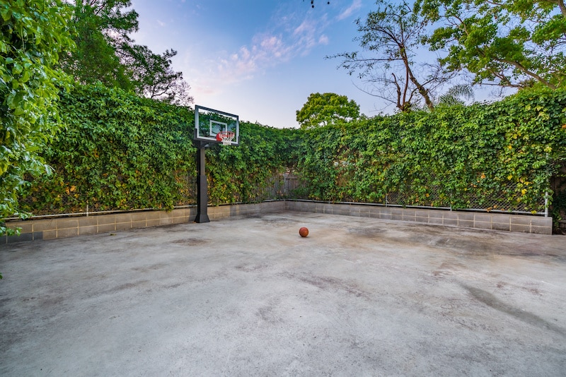 RHB Assets From IGX: Empty private concrete basketball court with surrounding fence and trees.