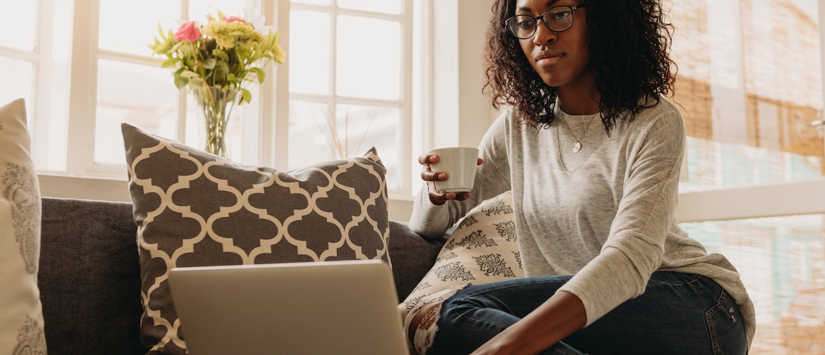 Woman on couch, evaluating credit her report online.