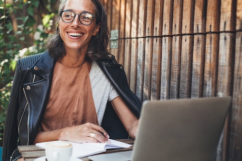 Woman smiling outside with notepad and laptop.