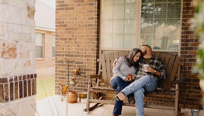 Couple sitting on wooden porch bench holding each other smiling.