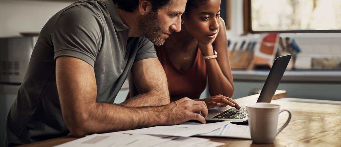 Couple at kitchen table with coffee looking over bills together.